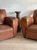 A pair of oversized French club chairs in original tan leather, deeply worn, with the rounded arms and low backs the form...