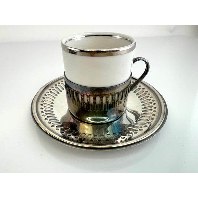 A refined vintage demitasse service featuring six porcelain cups with sleek silver rims, each nestled into sculptural...