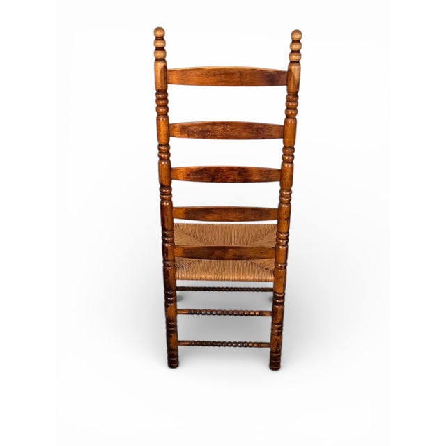 Charming antique ladderback chair featuring beautifully turned wood spindles, classic arched slats, and a handwoven rush...