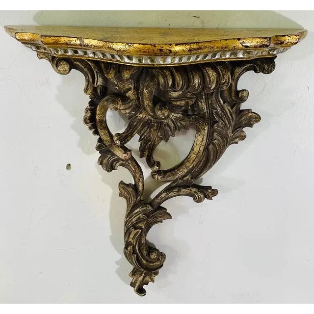 A pair of French Baroque style hand carved gesso and wood floral scroll design wall brackets featuring a scalloped gild...