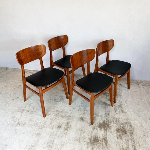 A set of four dining chairs with curved teak-veneered plywood backrests. Each back is cut from a sheet with strong figure,...
