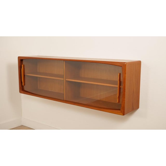 This vintage hanging sideboard is crafted from warm-colored teak wood. The piece features two glass sliding doors with...