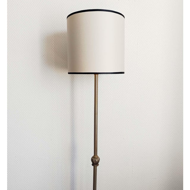 Gilt brass floor lamp, crafted in the classic style around 1950. It rests on three ornate foliage-shaped legs, with a...