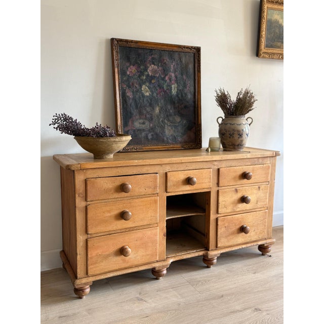 A long English pine knee-hole sideboard, the plank top worn to a warm honey colour over banks of drawers either side of a...