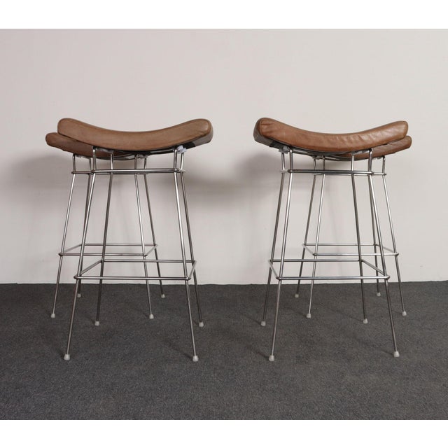 Set of four modern bar stools by Fernando Jaeger (ca. 1990s, Brazil). Composed of stainless steel frames with square foot...