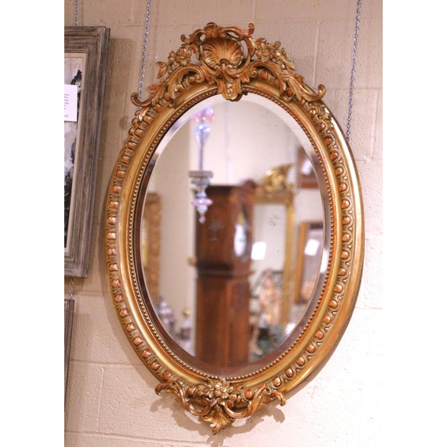 A refined antique French oval wall mirror crafted in carved giltwood circa 1860, showcasing the fluid and decorative...
