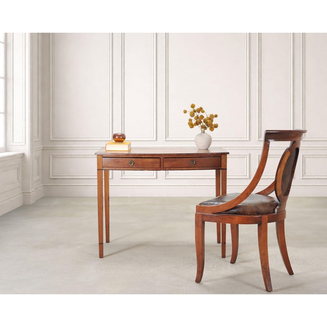 A handsome 19th century bow front side table or petite desk crafted in an English Regency style out of honey-amber...