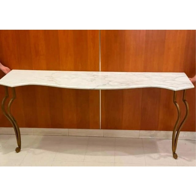 A large and genuinely dramatic console table with a scrolling gilt-iron base carrying a shaped white marble top with soft...
