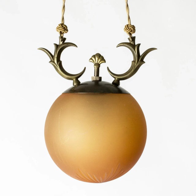 Lovely Swedish Grace ceiling light, with a brass and pale orange colored glass shade. Graphic, functionalist design....