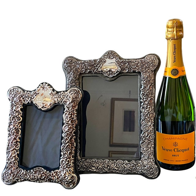 An ornate silverplated picture frame featuring elaborate scrolling foliage, small blossoms, lattice details, and a...