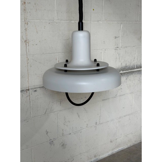 This white pendant light features a layered saucer shade with contrasting black accents, casting downward illumination....