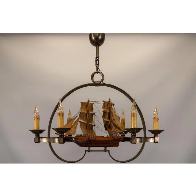 A rare french chandelier from the 1970s, featuring a hand-crafted wooden ship surrounded by six wrought iron candle...