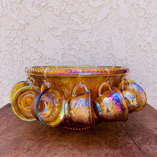 Lovely Mid Century Carnival glass punch bowl set. Consisting of 12 cups, 12 hooks and one bowl, the molded amber colored...
