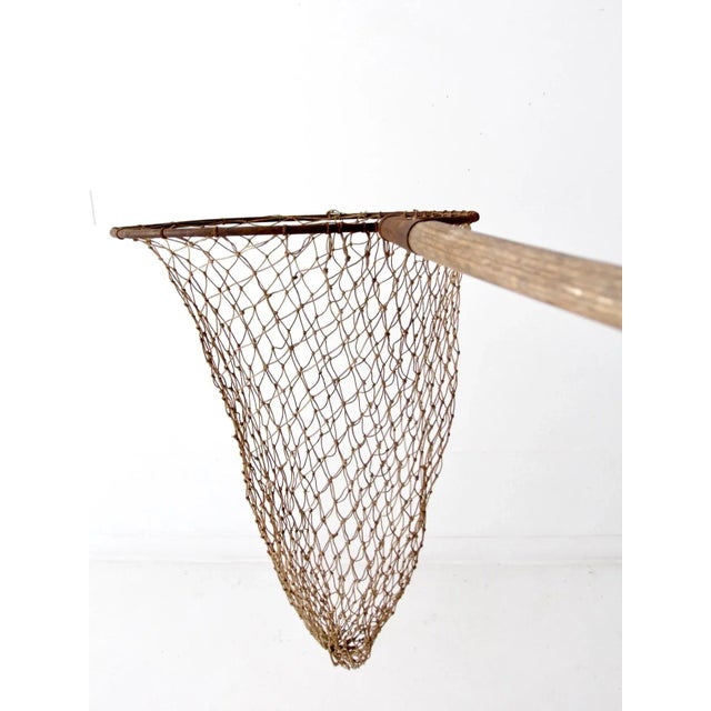 This is an antique fishing net on pole. The large hand held net features a wooden pole and metal frame with large woven...