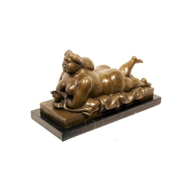 This solid bronze sculpture depicts a reclining nude woman on sheets, holding a cigarette in a pose of elegance and...