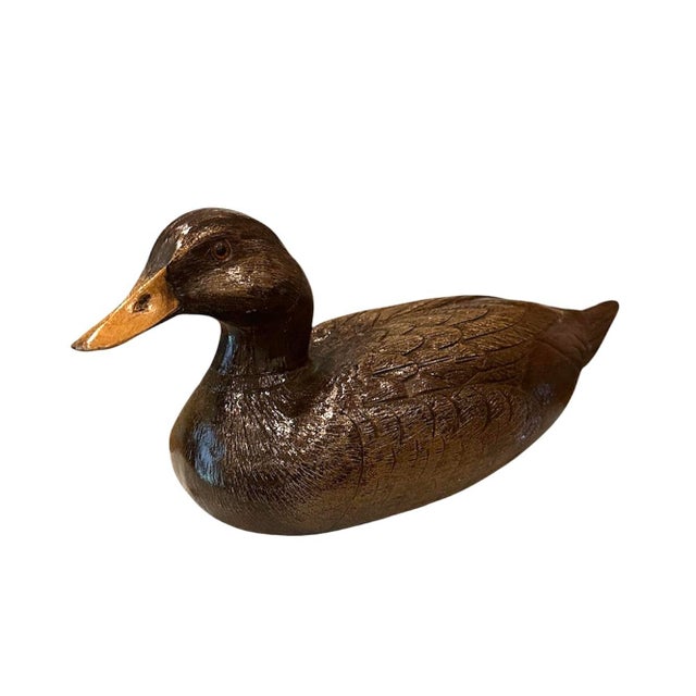 A vintage, hand carved duck decoy. Features a solid wood form with a two tone finish and amber colored eyes. Ochre colored...