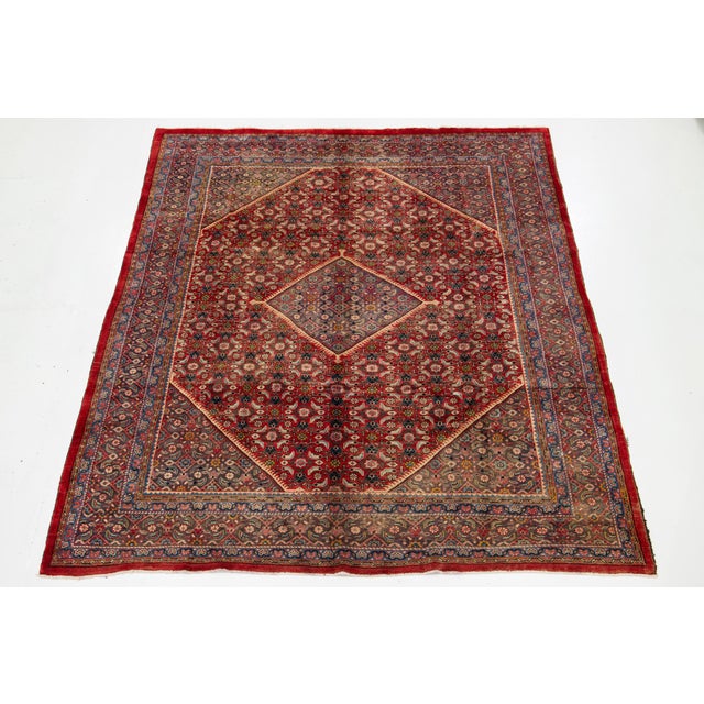 This Persian Mahal hand-knotted wool rug features a vibrant red field, beautifully complemented by multicolored accents...