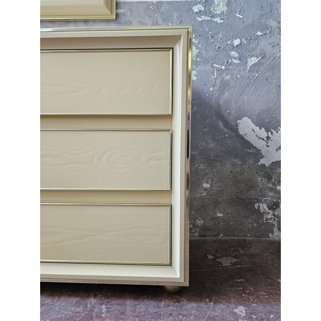 Splendid and elegant chest of drawers with mirror made in the 70s. Solid structure in beige lacquered wood with brass...