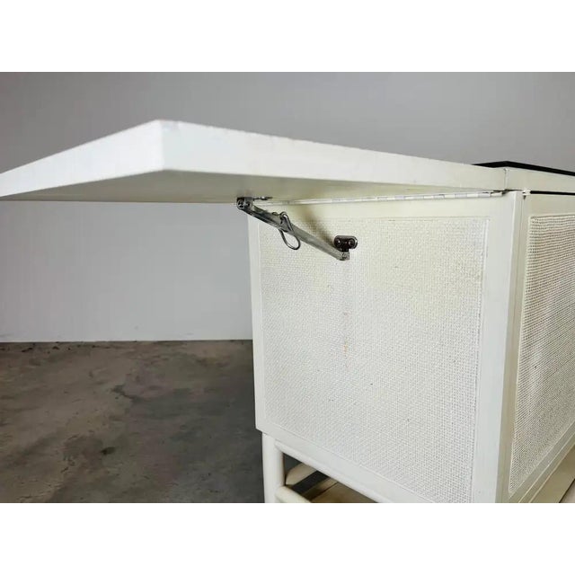 Mid-century drop-leaf server on casters having original white lacquer with cane front doors, ample cabinet storage and a...