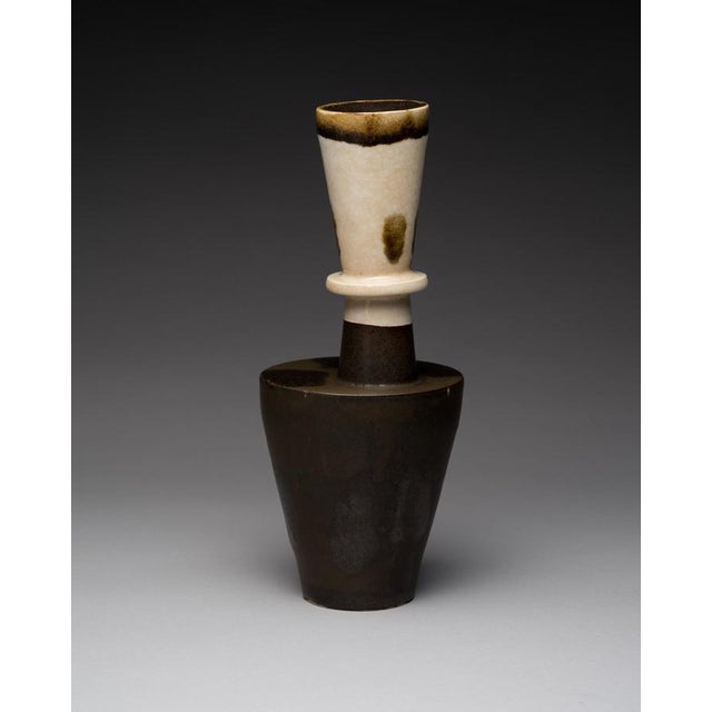 Tall German studio vase with a poised, totem-like silhouette in deep brown stoneware and a contrasting cream collar. The...