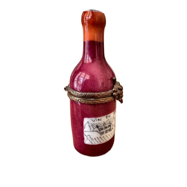 A charming vintage trinket box shaped like a bottle of Bordeaux wine, hand-painted in deep burgundy with a warm orange...