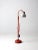 This is a vintage industrial floor lamp. The work lamp features an orange metal base and frame with an aluminum shade. It...