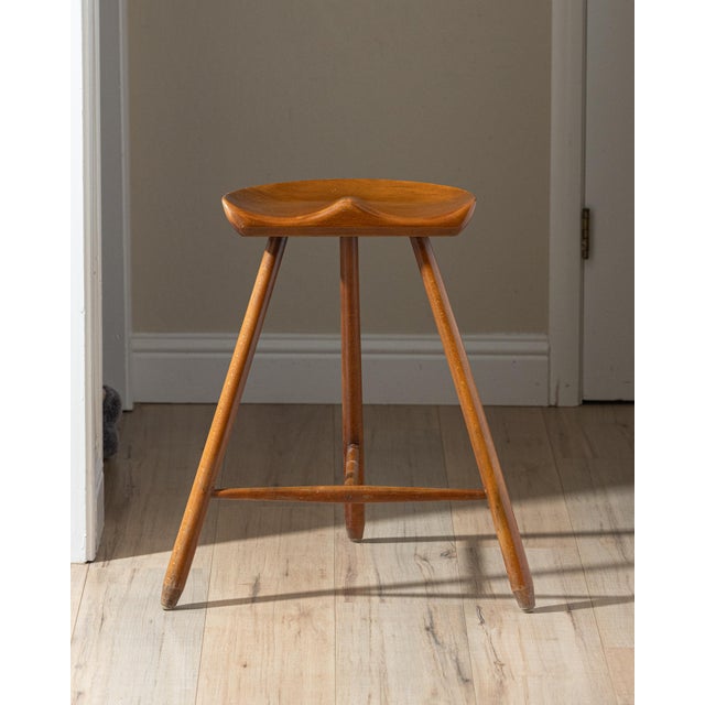 Sculptural vintage tripod stool crafted from solid beech, featuring a carved saddle-form seat, tapered legs, and slender...