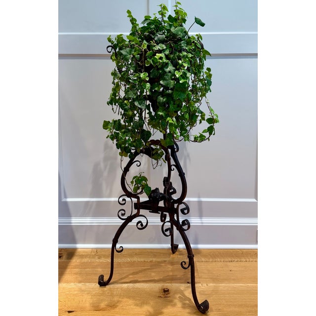 A Continental wrought iron tripod plant stand with an open, sculptural form composed of scrolling ironwork and hand-worked...