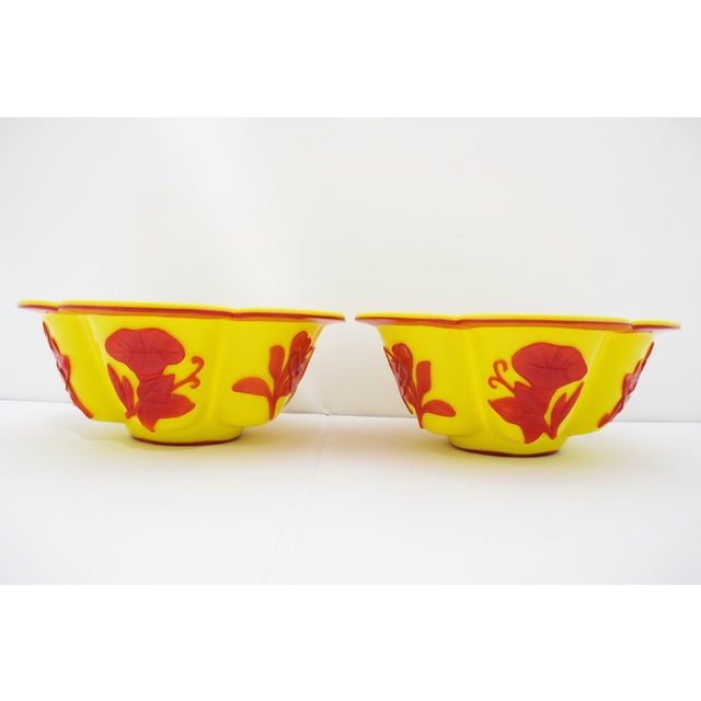 Pair of Chinese imperial yellow Peking glass bowls. Each features foliate lotus-lobed edges and striking carved red floral...