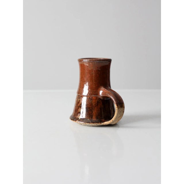 This is a vintage studio pottery mug. Signed by the artist, the handmade mug has a beautiful russet brown glaze.