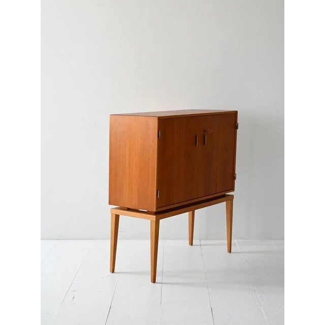 A 1950s teak tv cabinet converted into a bar, with its original frame, interior mirrors, and brass handles. a vintage...