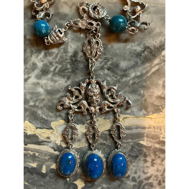 This vintage ornate silver necklace features intricate scrollwork links and a richly detailed central pendant, reflecting...