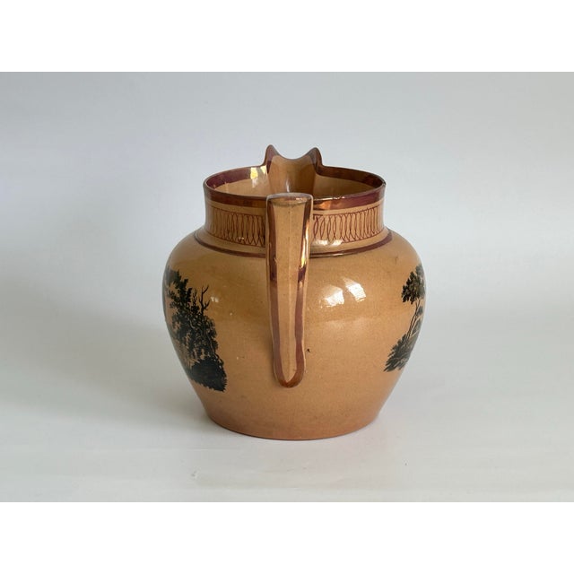 An antique English lustreware pitcher, attributed to Sunderland, featuring black transfer-printed landscape scenes of...