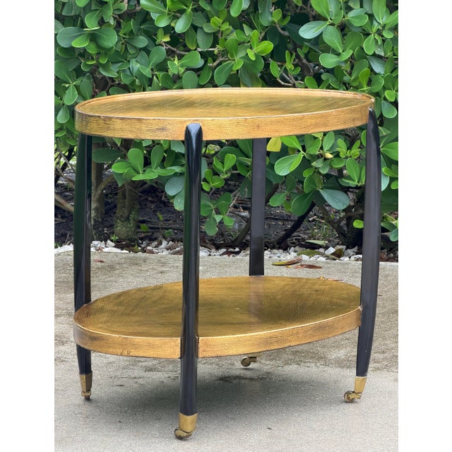 Two-tier oval bar cart featuring a highly decorative painted gold finish with a distinctive faux-grain pattern across both...