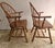 A Pair of Mid-Century Windsor Style Oak Captain Chairs Measures 25" in width, 22" in depth and 37" in height with a 18"...
