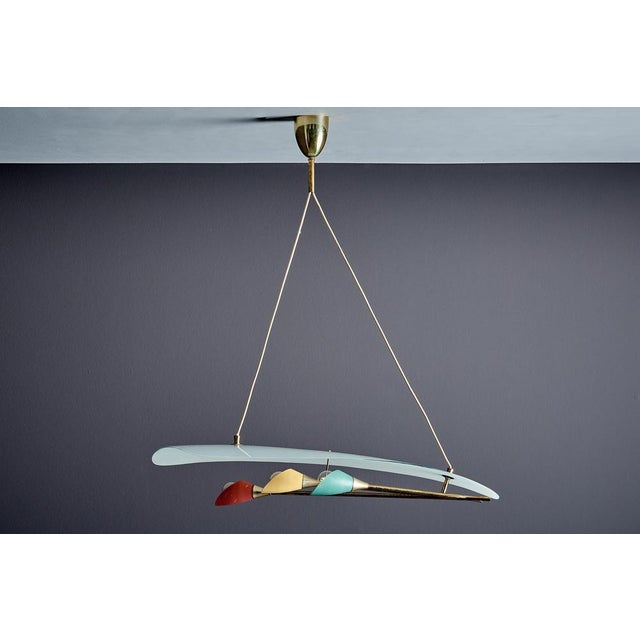 A sculptural 1950s Italian pendant with a sweeping frosted glass shade, brass structure, and three playful colored...
