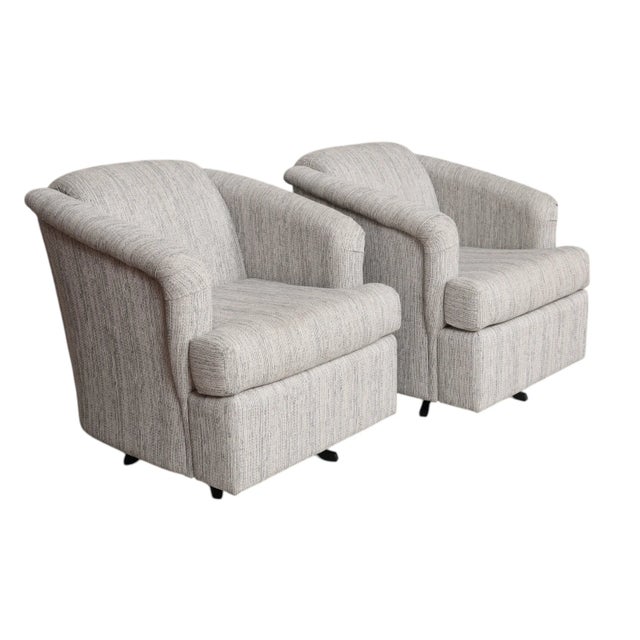 A pair of contemporary style swivel club chairs upholstered in a gray basketweave fabric. Saddle arms frame a square seat...