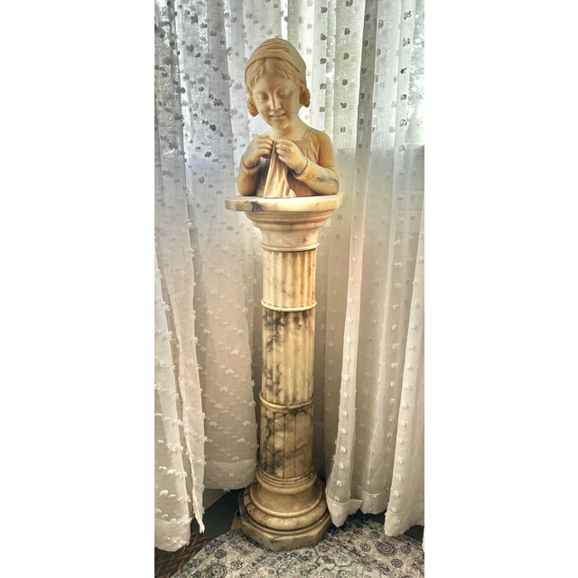 An exceptional late 19th–early 20th century Italian alabaster bust depicting a young girl absorbed in the quiet act of...