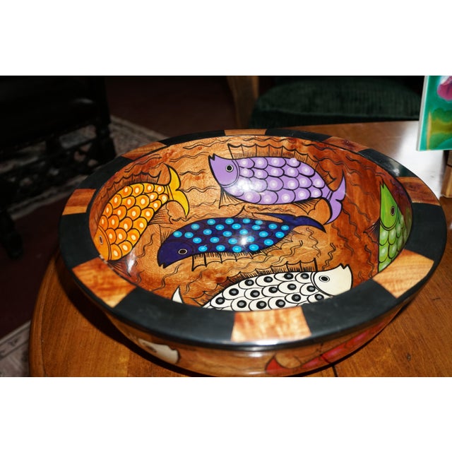 A vibrant and whimsical decorative wooden bowl featuring an eye-catching collection of colorful fish swimming across a...