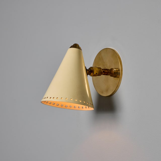 1950s Stilnovo White Perforated Metal Sconce Executed in cream painted perforated metal shade with brass arm and...