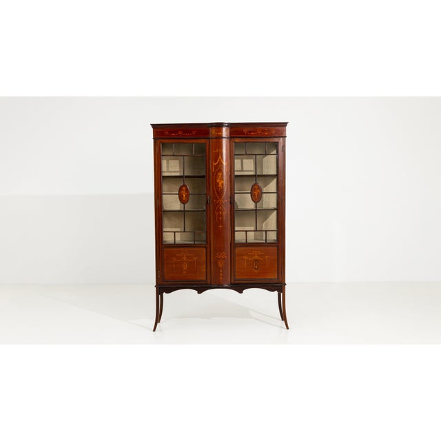 An elegant Edwardian vitrine showcasing detailed marquetry work and refined proportions. The glass panels allow for the...