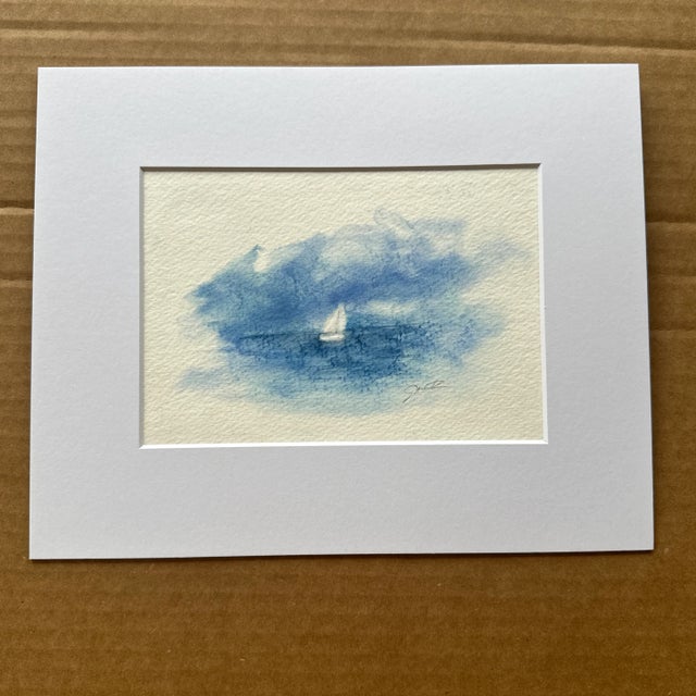 This delicate, dreamlike painting features a single white sailboat drifting in a serene sea of blue. Soft brushwork and...