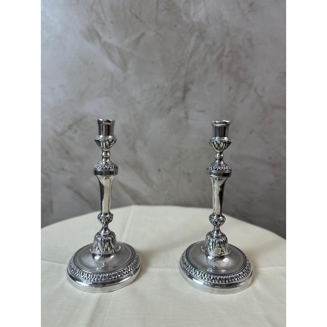 A charming pair of silver-plated metal candlesticks dating from the early 20th century, inspired by the Louis XVI...