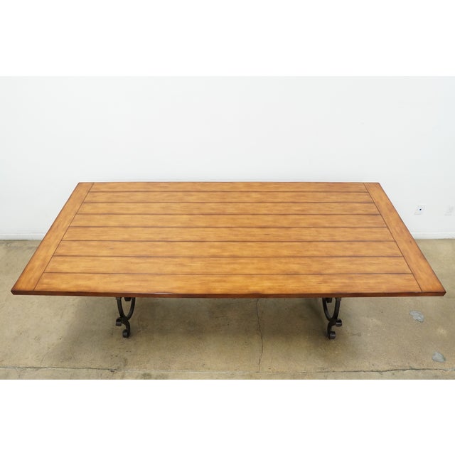Vintage dining table featuring a warm wood top and an ornate iron base with dramatic scrollwork detailing. The rectangular...
