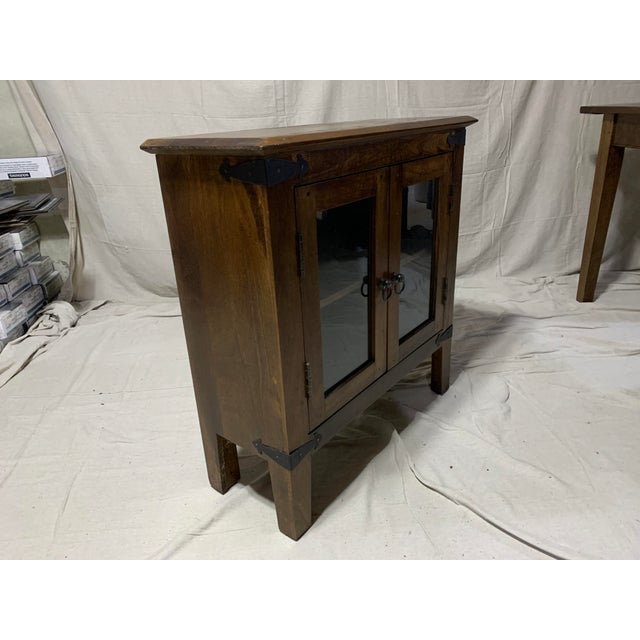 Solid wood cabinet with glass doors and finished with a dark walnut stain. Corners are adorned with iron plates and door...