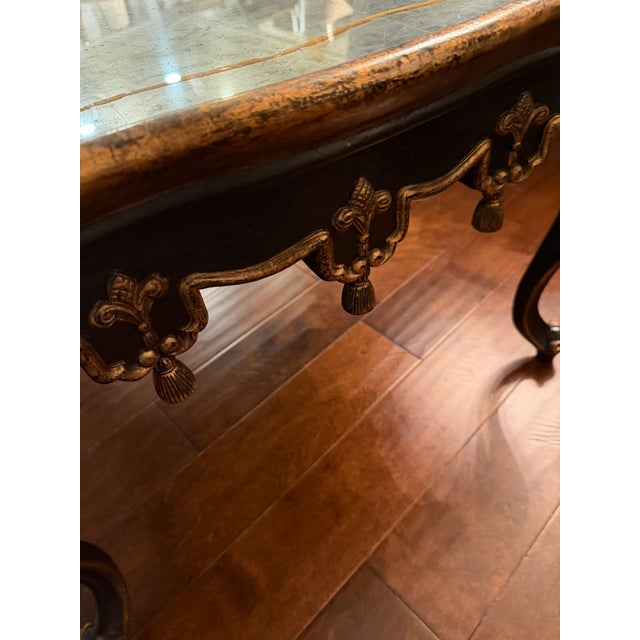 1980’s coffee table with antiqued mirror top with delicate gold-leaf trim and a gracefully scalloped dark wood frame