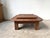 A tiered coffee table in solid oak, in a modernist and brutalist style, circa 1970. Its architectural lines are...