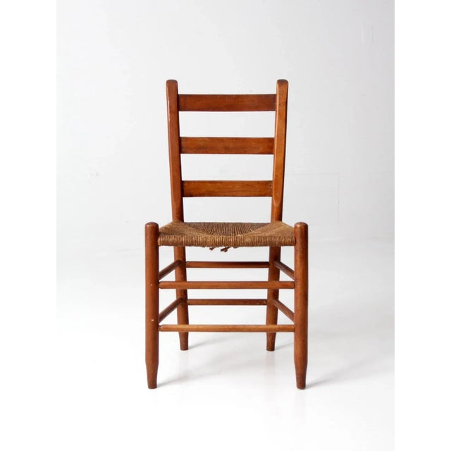 An antique ladder-back chair in a classic French country style, featuring a clean ladder back and woven rush seat. The...