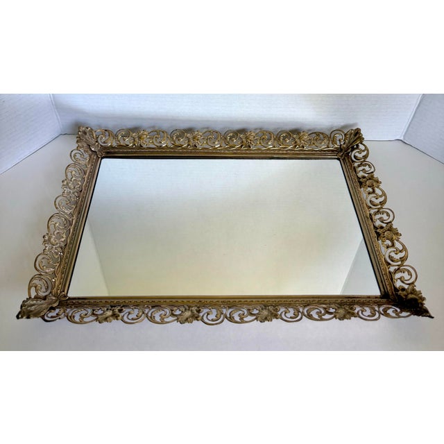 Dating to the mid-20th century, this elegant Hollywood Regency mirror features a beautifully pierced gold-tone metal frame...