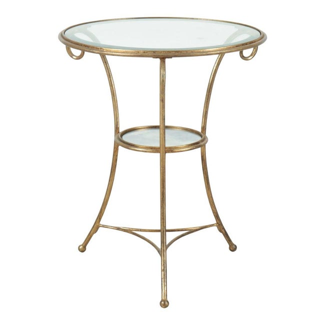 An elegant vintage round gueridon table featuring a clear glass top set within a slender gilt metal frame. The graceful...
